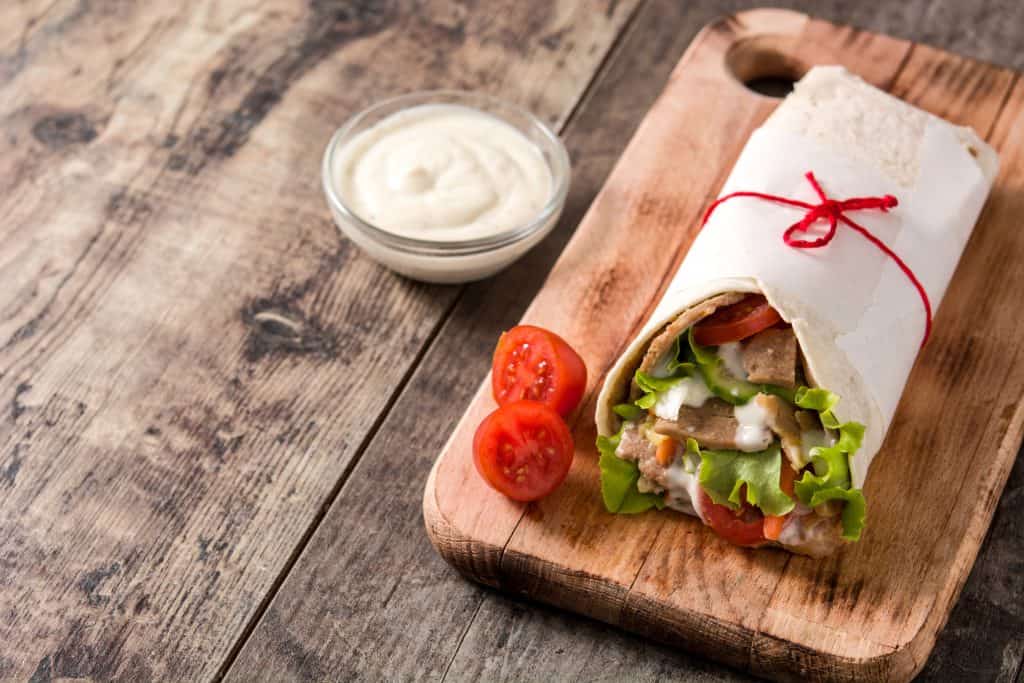Salsa blanca de kebab junto a un kebab servido en una mesa de madera