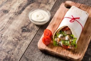 Salsa blanca de kebab junto a un kebab servido en una mesa de madera